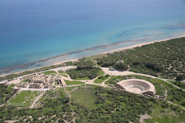 Aerial view of ancient stone ruins and an amphitheater along a turquoise Mediterranean coastline.