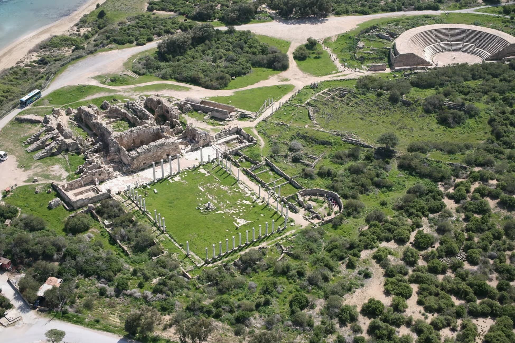 Aerial view of ancient stone ruins featuring a columned courtyard and a large semicircular amphitheater.